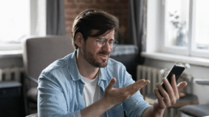 A man looking frustrated and confused while trying to use a poorly designed website on his smartphone, illustrating the need for mobile-first design.