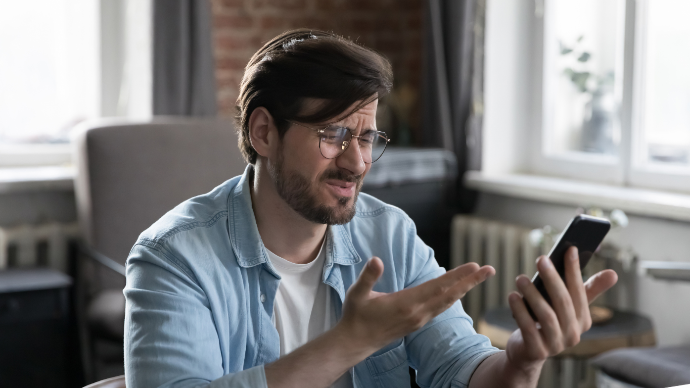 A man looking frustrated and confused while trying to use a poorly designed website on his smartphone, illustrating the need for mobile-first design.