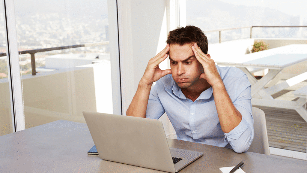 A frustrated man sitting at a laptop with his head in his hands, symbolizing confusion and high bounce rate caused by poor website user experience (UX).