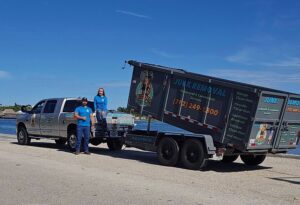 Junk removal team posing with branded hauling truck and trailer, offering residential and commercial cleanup services.